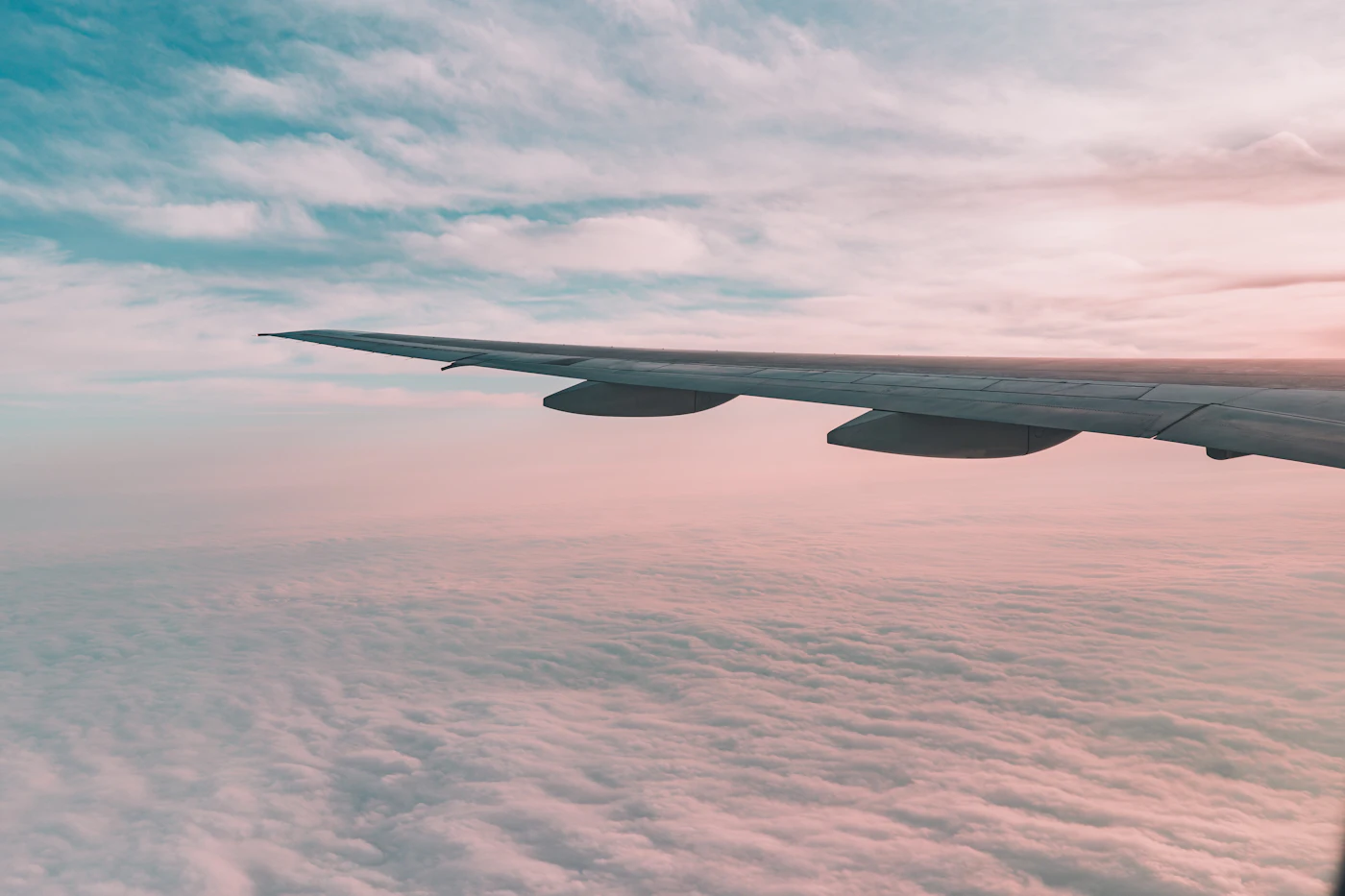 An airliner's wing above a sea of pink cloud at dawn